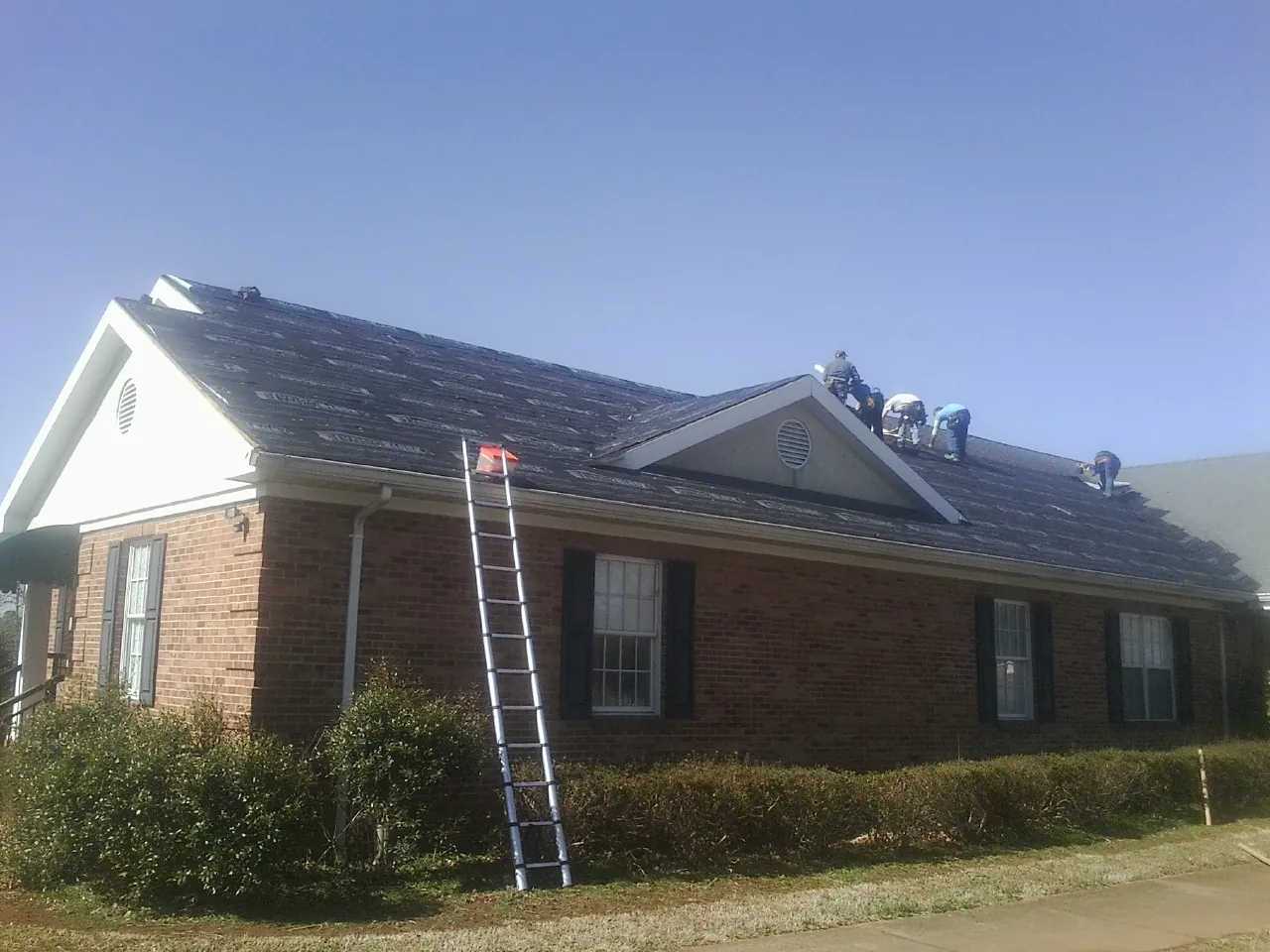 Crew tearing shingles off a brick ranch roof with a ladder set — Emergency Roof Repair work by our crew in Browerville