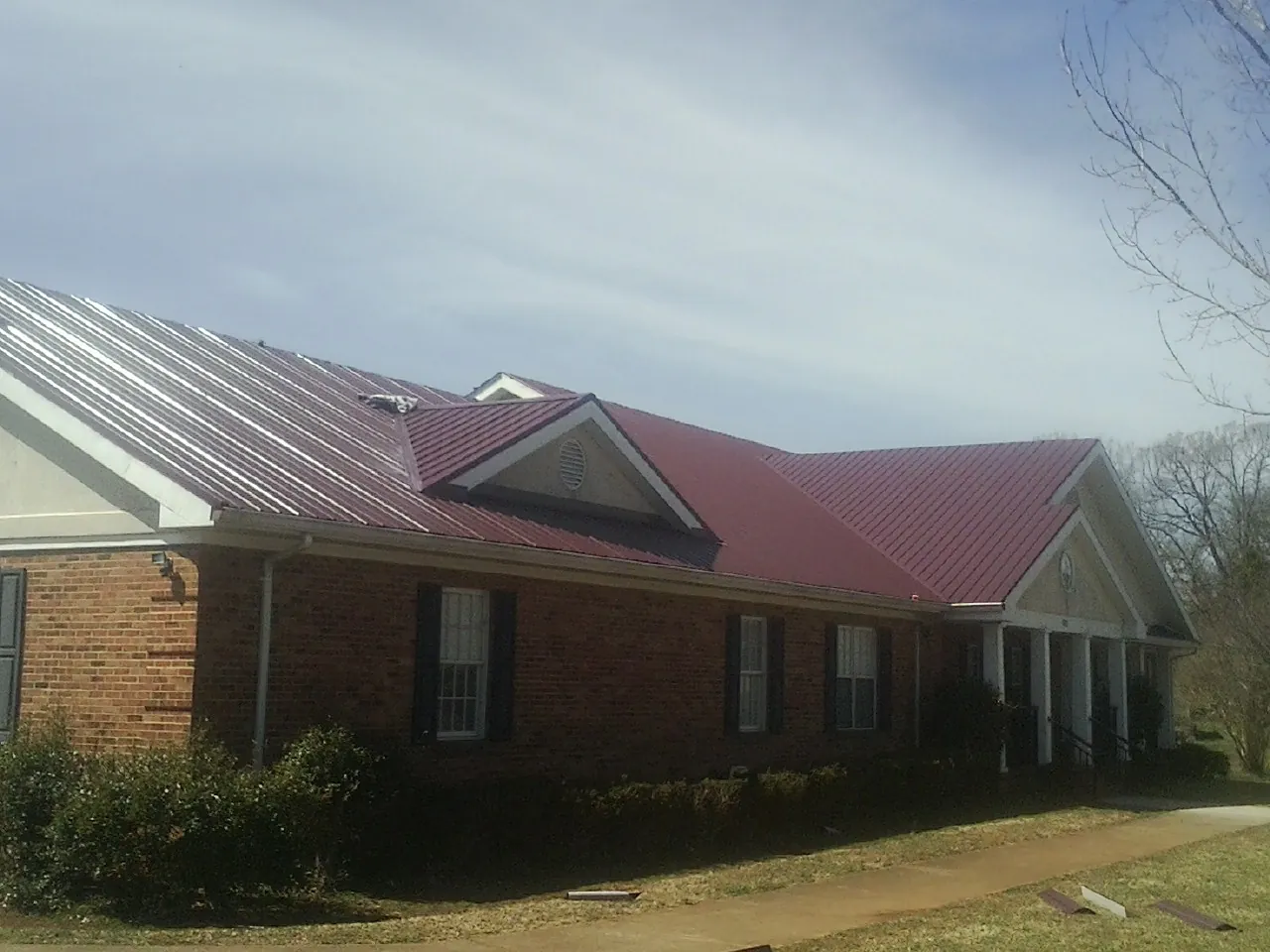 Red metal roof with gabled entries on a long brick building, from a Hail Damage Roof Repair job in Browerville