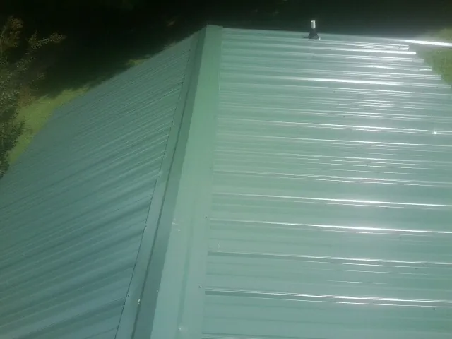 New green metal panels meeting at the ridge of a roof — Flat Roof Repair work by our crew in Browerville