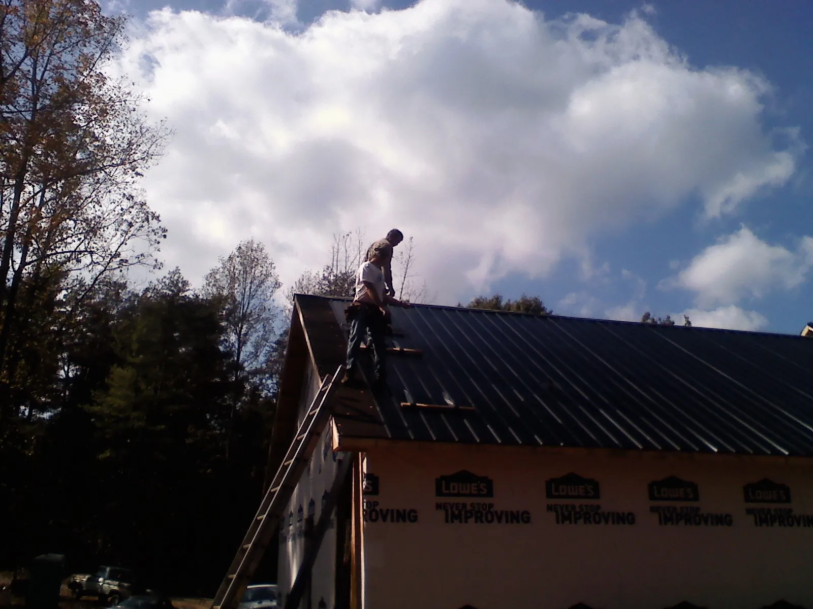 Roofer fastening dark metal panels high against a cloudy sky, from a Roof Inspection job in Browerville