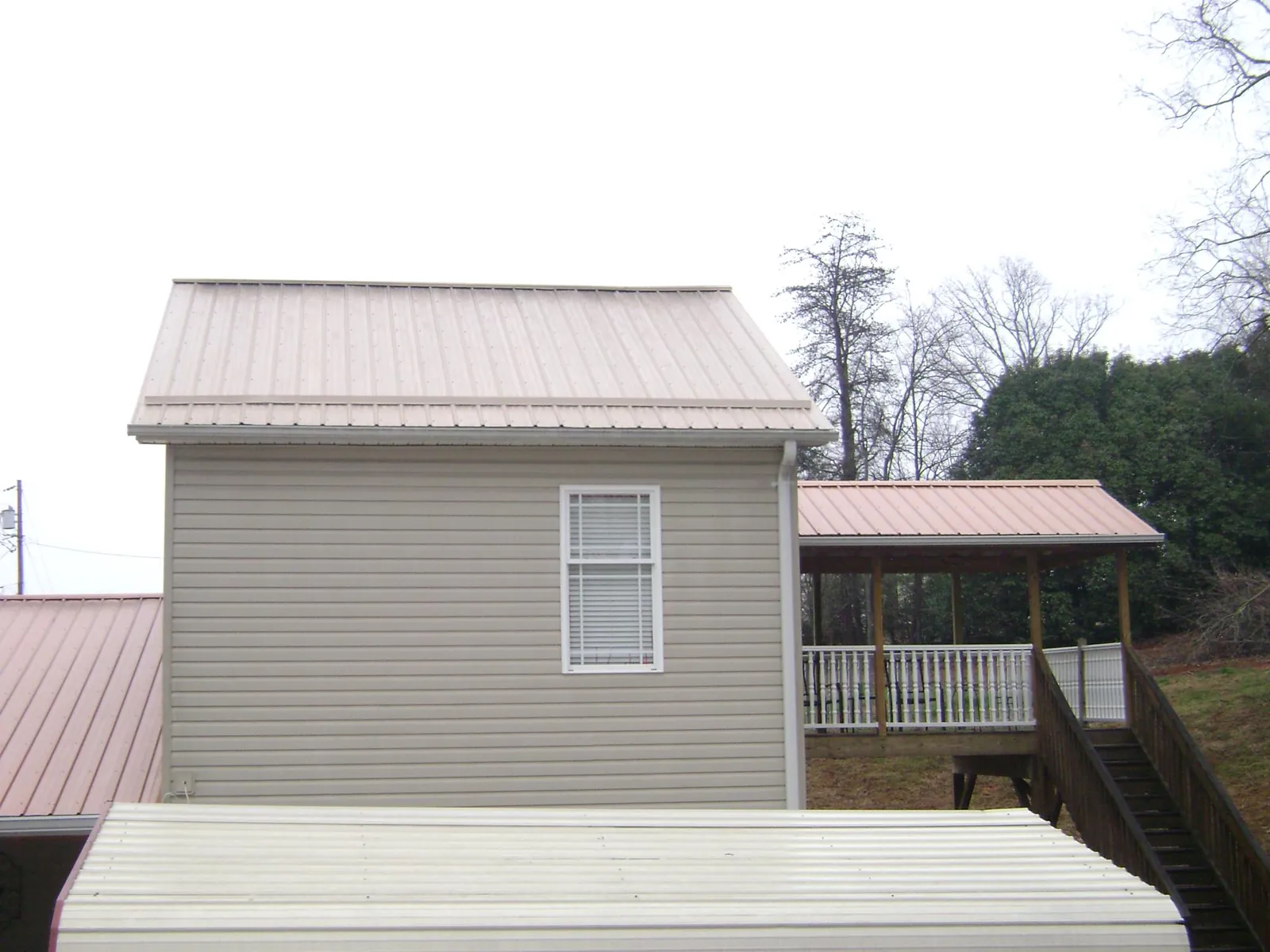 Tan metal roofs on a two story addition and attached porch, from a Roof Replacement job in Browerville